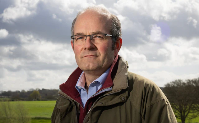 User-supplied photograph identified as Tom Bradshaw, standing outdoors beside farmland